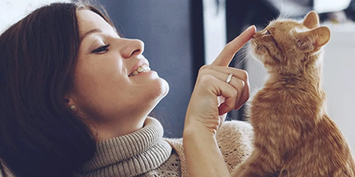 A smiling woman touching noses with her orange tabby cat on the couch